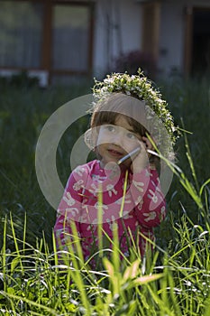 Beautiful little girl with flowers head wreath and talking on her cell phone in the park