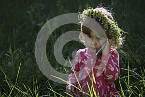 Beautiful little girl with flowers head wreath and talking on her cell phone in the park