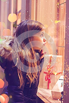 Beautiful little girl in front of confectionery shop, decorated with wrapped gift boxes and candies. Christmas concept, window