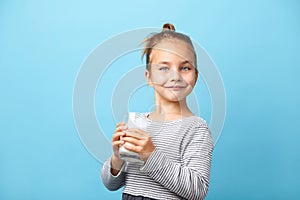 Beautiful little girl with glass of milk, stands on blue isolated.