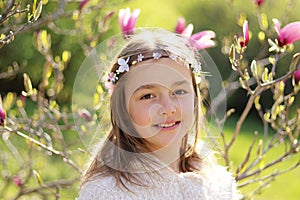 Beautiful little girl with handmade hair wreath on her head smiling looking at camera in the blooming spring garden