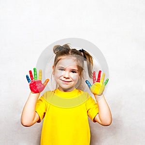 Beautiful little girl with hands in paint smiles in a yellow T-shirt. Children`s creativity.