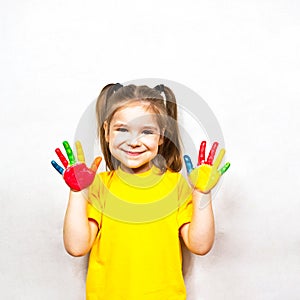 Beautiful little girl with hands in paint smiles in a yellow T-shirt. Children`s creativity.