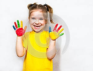 Beautiful little girl with hands in paint smiles in a yellow T-shirt. Children`s creativity.
