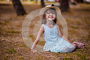 Beautiful little girl in a hat and white dress girl sitting on the lawn and laughing on a beautiful autumn warm day.