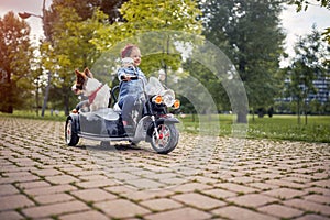 Beautiful  little girl having fun while driving electrical motorcycle with sidecar and her dog in park