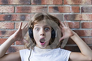 beautiful little girl with headphones at home listening to music and having fun, technology and music concept. Brick background