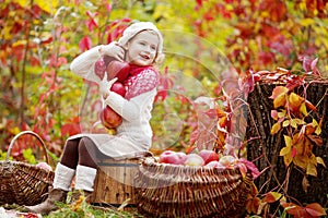 Beautiful little girl holding apples in the autumn garden. . Little girl playing in apple tree orchard. Toddler eating fruits at