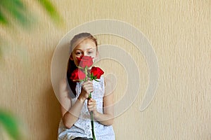 Beautiful little girl holding a bouquet of red roses on a beige background. Playing hide and seek. Copy space.