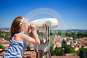 Beautiful little girl looking at coin operated binocular on terrace at small town in Tuscany, Italy