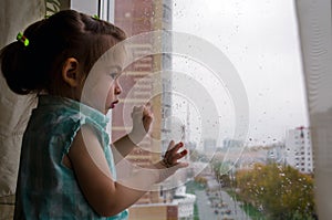 beautiful little girl looking out the window in the rain