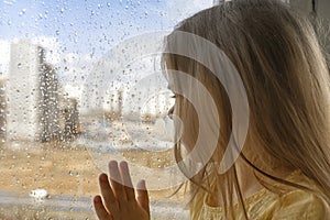 beautiful little girl looks out the window at the rain. stay home
