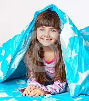 Beautiful little girl lying in bed under a blue blanket