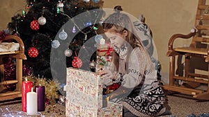 Beautiful little girl near a Christmas tree opens a gift box with a New Year`s gift from Santa Claus