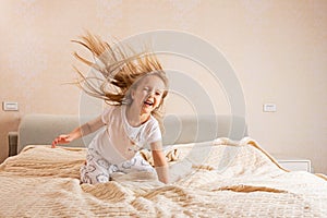 Beautiful little girl in pajamas jumping on the bed at home. Stay at home during coronavirus covid-19 lockdown and have