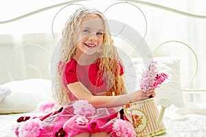 Beautiful little girl in pink dress sitting on the bed