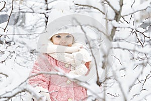 Beautiful little girl in a pink fur coat and a knitted hat among the snow-covered trees