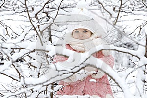 Beautiful little girl in a pink fur coat and a knitted hat among the snow-covered trees