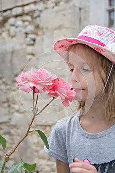 Beautiful little girl in pink straw bonnet smelling pink rose