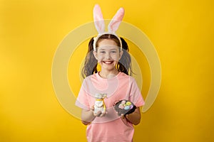Beautiful little girl in a pink t-shirt with rabbit ears holds a nest with Easter eggs and a toy rabbit