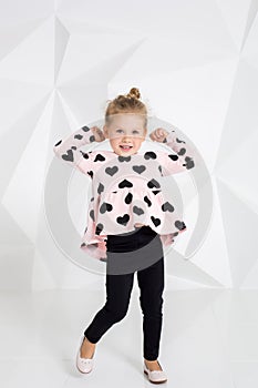 Beautiful little girl in a pink tunic with black hearts and leggings posing in front of camera in studio