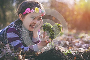 Beautiful little girl planting a heart-shaped tree and dreaming of a beautiful future