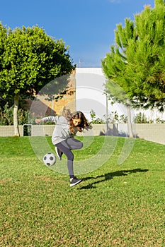 Beautiful little girl playing soccer in a nice park with natural grass on a sunny winter day. Copy space