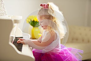 Beautiful little girl is playing on a white grand piano.