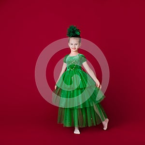 Beautiful little girl princess dancing in luxury green dress isolated on red background. Carnival party with costumes