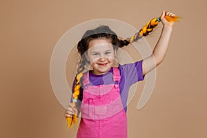 Beautiful, little girl, pulling kanekalon pigtails of yellow color, looking at camera with gentle smile, wearing pink