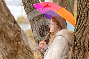 Beautiful little girl with rainbow colored umbrella dreaming staying near the tree outside