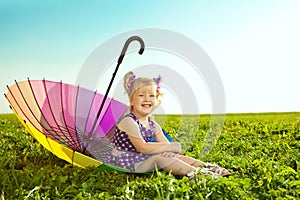 Beautiful little girl with rainbow umbrella on the grass in the