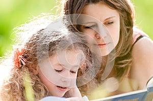 Beautiful little girl reading book with ger mother