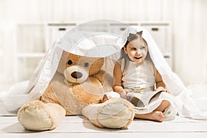 Beautiful little girl reading to her teddy bear toy