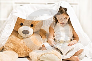 Beautiful little girl reading to her teddy bear toy