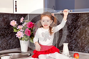 Beautiful little girl in a red skirt sits at the kitchen table in the interior