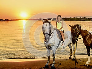 Beautiful little girl riding horse in sunset by the sea on the