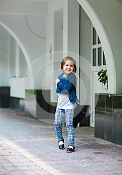 A beautiful little girl, a schoolgirl, in the afternoon near the school, in a school uniform