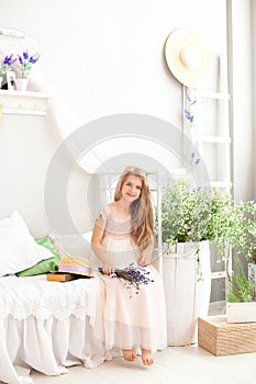 Beautiful little girl sits on a bed in a bright white bedroom with a rustic interior. Childhood concept. Provence style bedroom, c