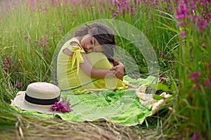 A beautiful little girl, sits hugging her knees and closing her eyes, in a yellow dress