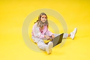 Beautiful little girl sitting on a light floor with a gray laptop and smiling, empty space