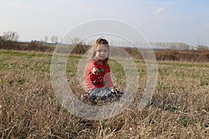 Beautiful little girl is sitting in the meadow