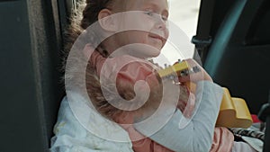 Beautiful little girl sitting in an open trunk of a car on the river bank of the sea playing on a yellow ukulele