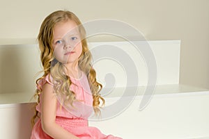 Beautiful little girl is sitting on the white staircase.