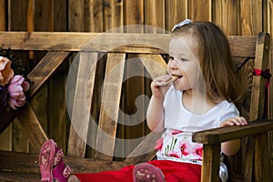 Beautiful little girl sitting on a wooden bench and have a cookie.