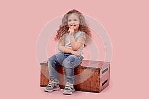 Beautiful little girl sitting on a wooden pedestal shows a gesture of silence.