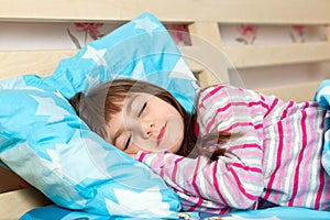 Beautiful little girl sleep in bed under a blue blanket