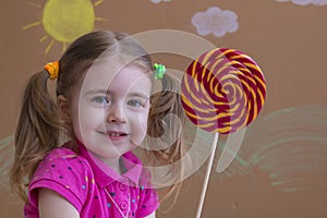 Beautiful little girl smiles with lollipop, happy little girl eating big sugar lollipop.