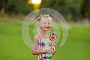 Beautiful little girl with smiling eyes with colored lollipop.