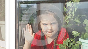 Beautiful little girl smiling and watching out the window. A child looks out the window. Portrait of cheerful kid. self